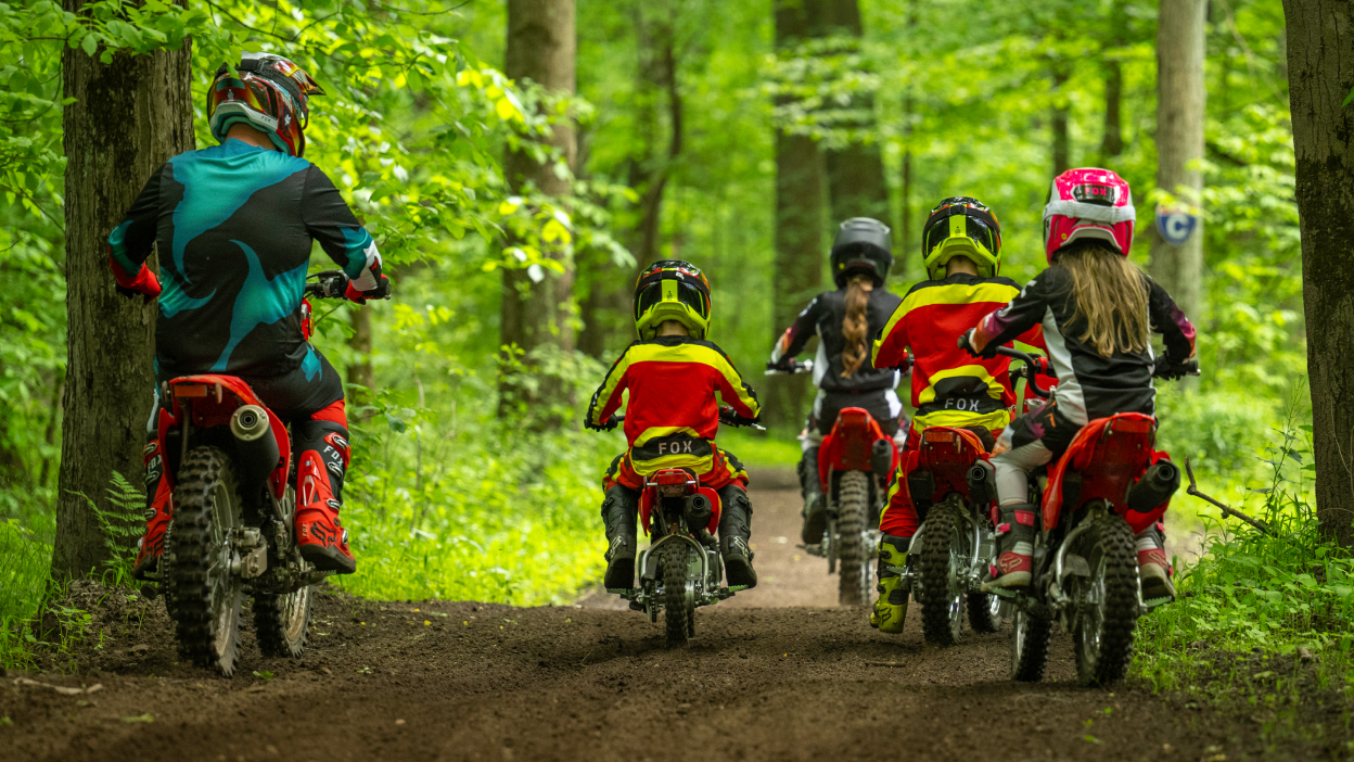 Rear view of two adult riders and three young drivers on dirt track in forest.