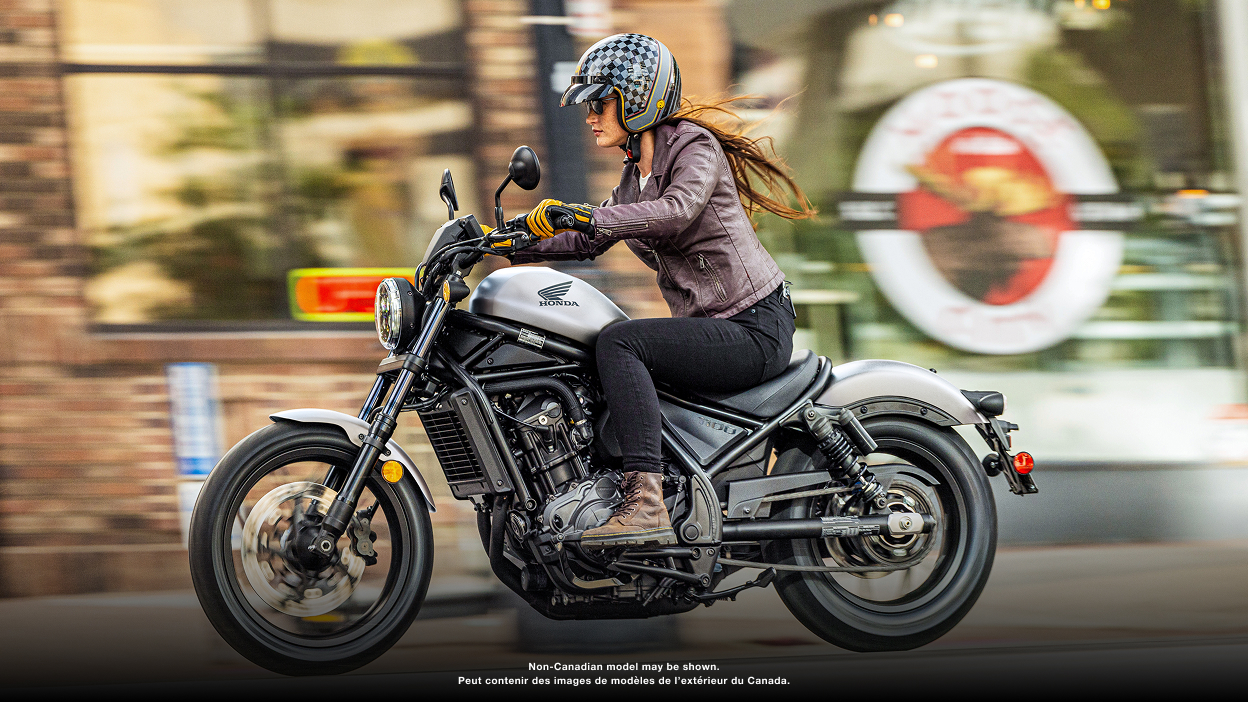 Rider turning right on street. Buildings and parked car in background. Accessorized model shown