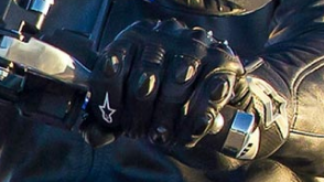 Close up of a hand in a black leather glove gripping the controls of a motorcycle. / Gros plan d'une main dans un gant de cuir noir saisissant les commandes d'une moto.